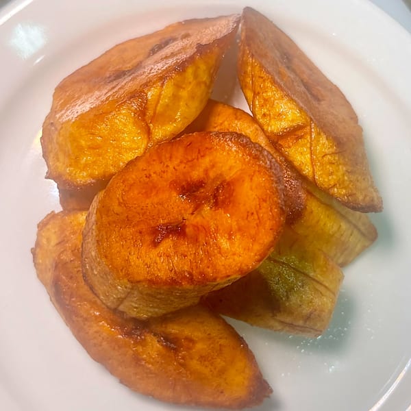 A white plate holds several slices of golden-brown fried plantains, a popular African-fusion side dish.