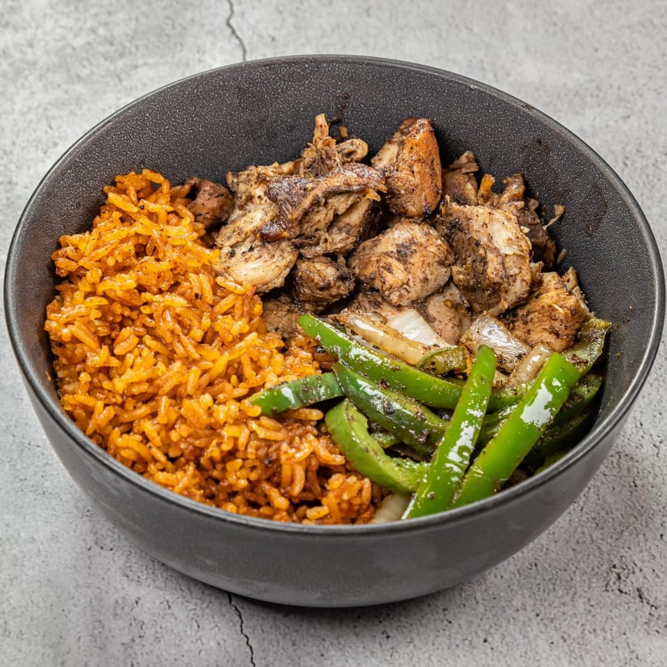 A Jungle Plate bowl with jollof rice, seasoned chicken, and green bell peppers.