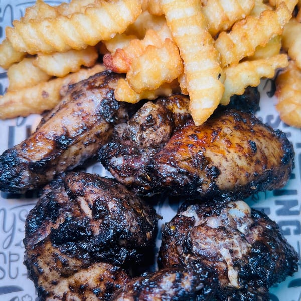 Close-up of The Jungle Plate's grilled chicken wings with crispy crinkle-cut fries.