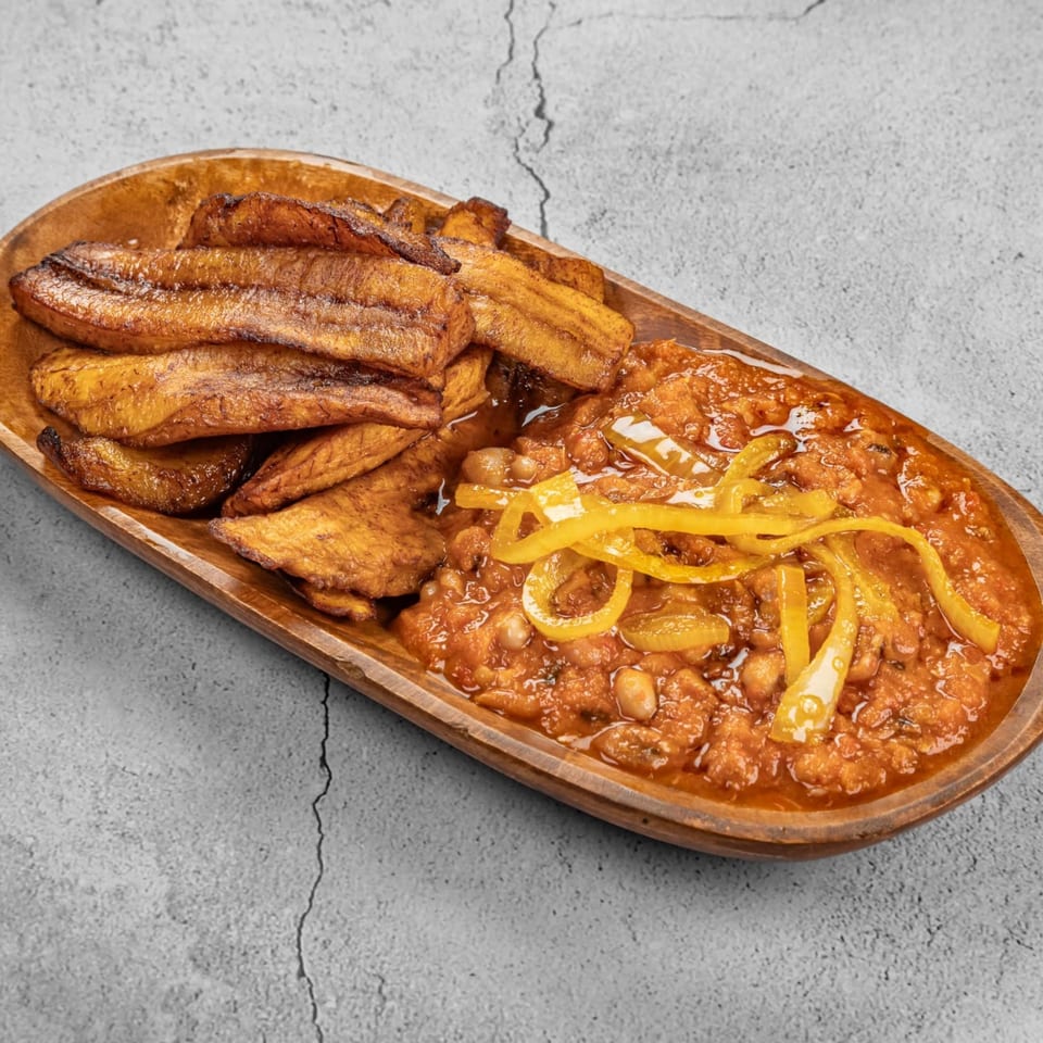 African-fusion dish with fried plantains and a bean stew topped with yellow peppers in a wooden bowl.