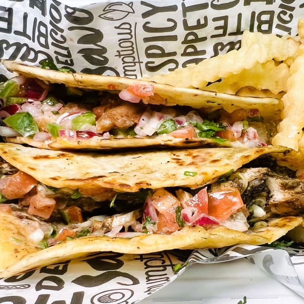 Two African-fusion quesadillas with chicken, salsa, and fries in a branded paper-lined basket.