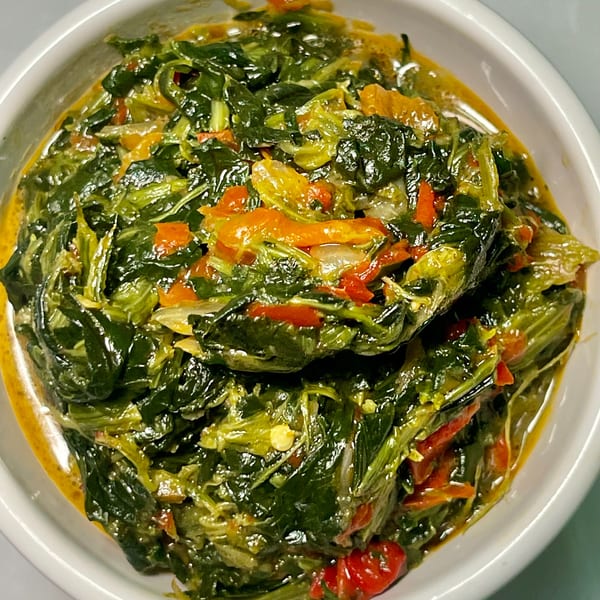 Close-up of a vibrant green African-fusion spinach dish with red and yellow peppers in a white bowl.