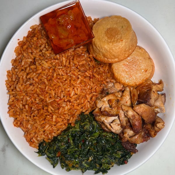 The Jungle Plate's Jollof rice, stewed greens, fried plantains, and grilled chicken in a white bowl.