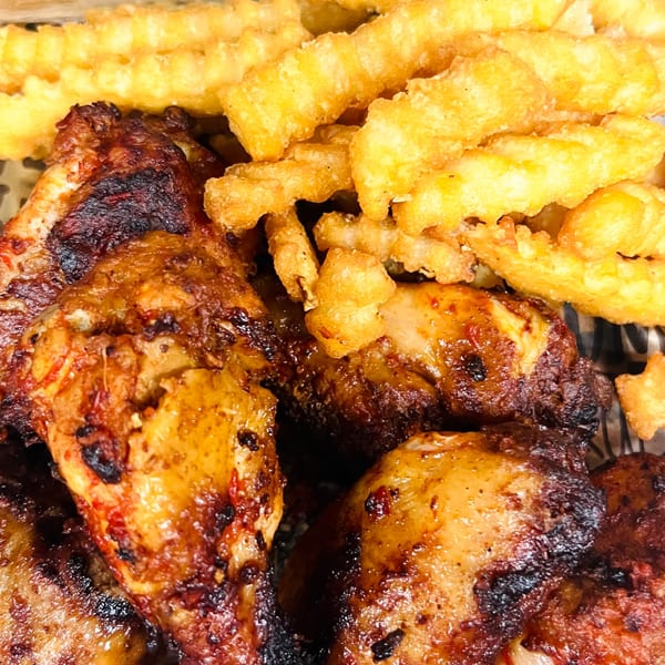 Close-up of grilled African-fusion chicken wings with crispy crinkle-cut fries.