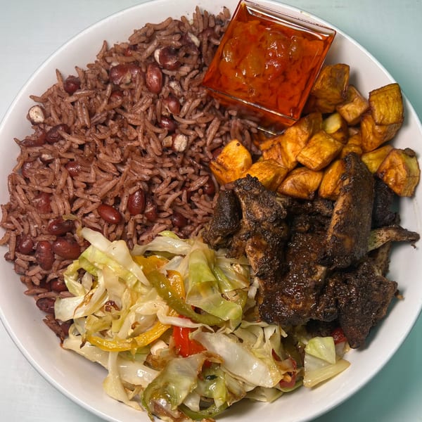 A white bowl filled with red rice and beans, fried plantains, stewed cabbage, and dark grilled meat.